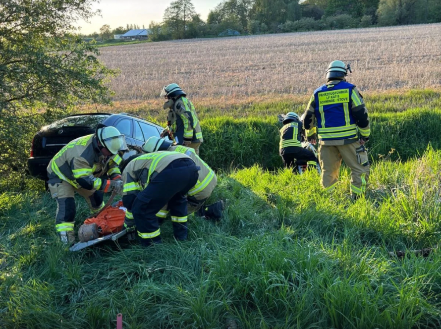 Feuerwehrleute um einen PKW im Graben