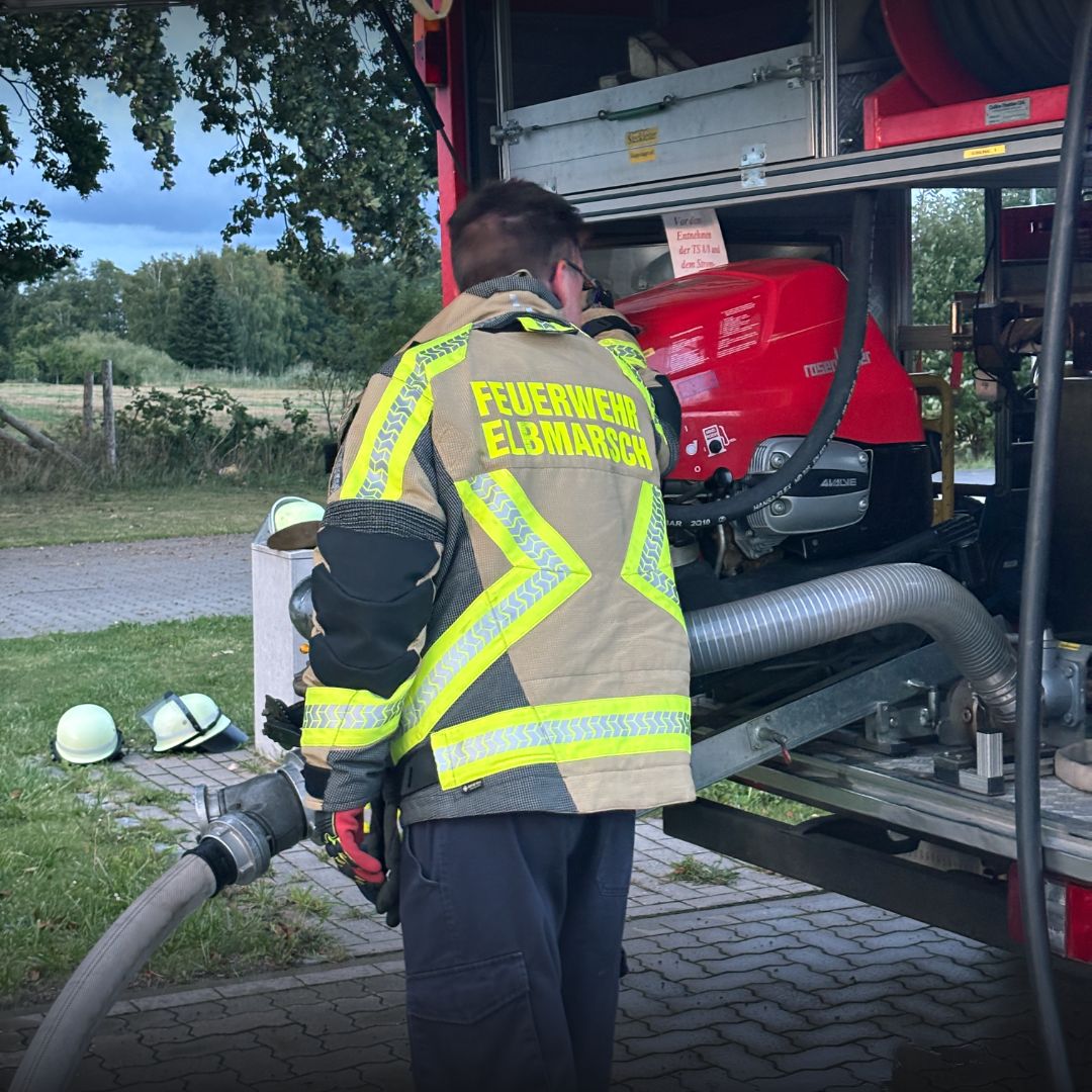Feuerwehrangehörige in Einsatzkleidung neben einem Feuerwehrfahrzeug