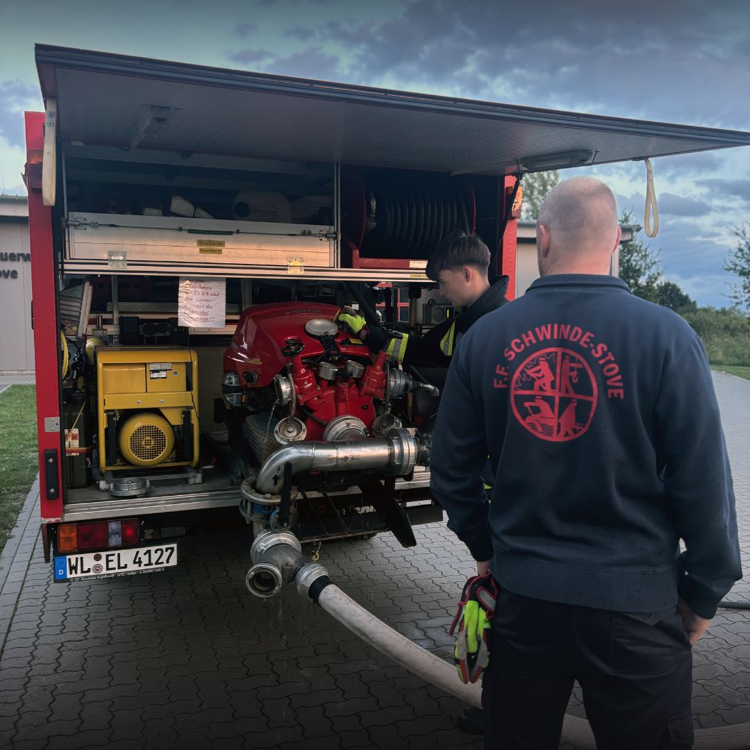 Feuerwehrangehörige stehen neben einem Feuerwehrfahrzeug und technischer Ausrüstung