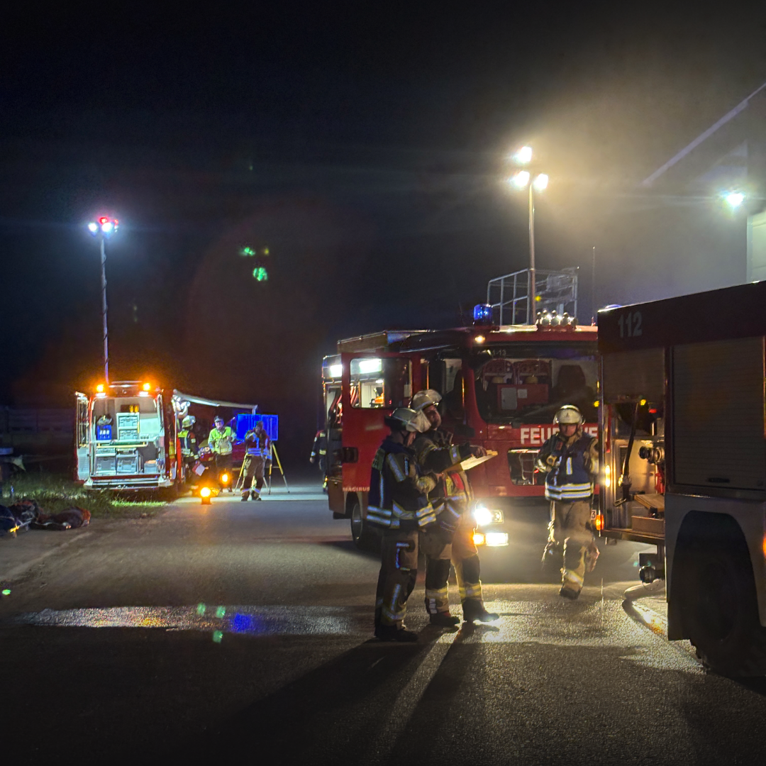 Mehrere Löschfahrzeuge stehen nachts auf einem ausgeleuchteten Betriebshof, im Vordergrund sprechen zwei Einsatzkräfte miteinander.