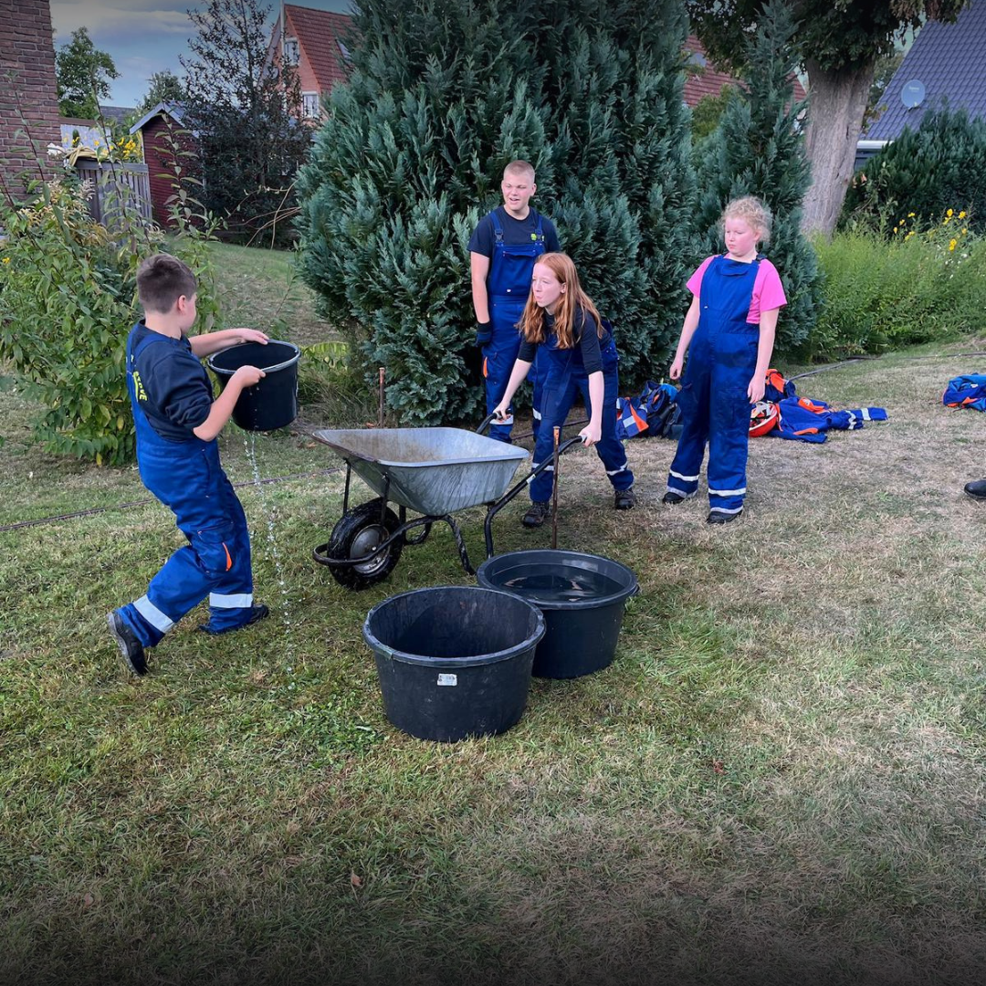 Kinder transportieren Wasser mit Eimern und einer Schubkarre