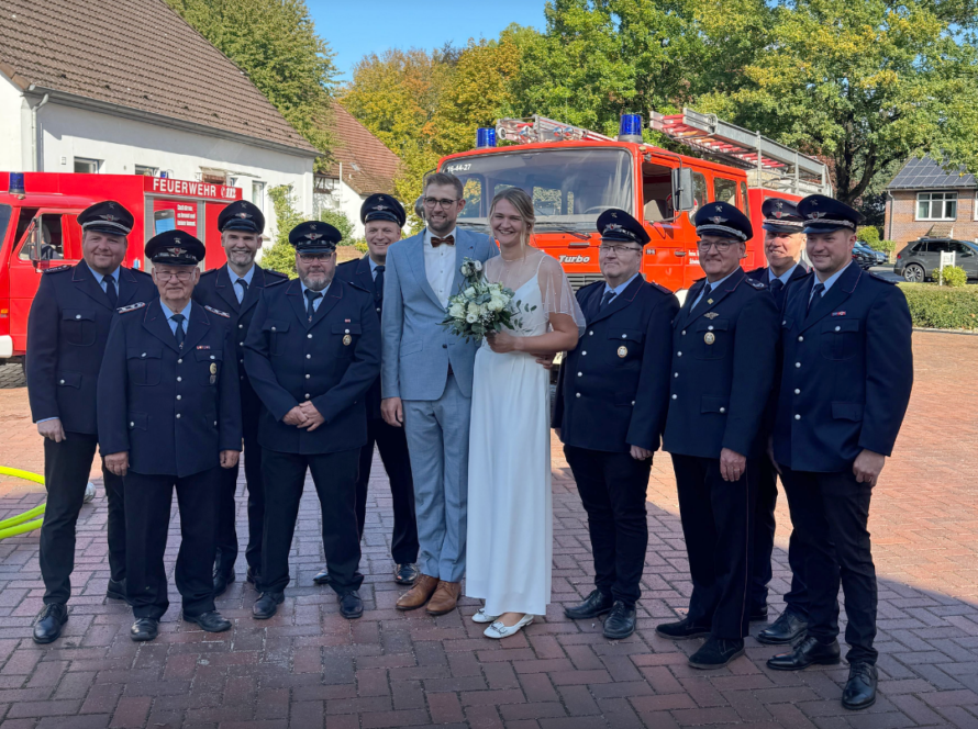 Brautpaar mit Feuerwehrkameraden vor den Feuerwehrfahrzeugen